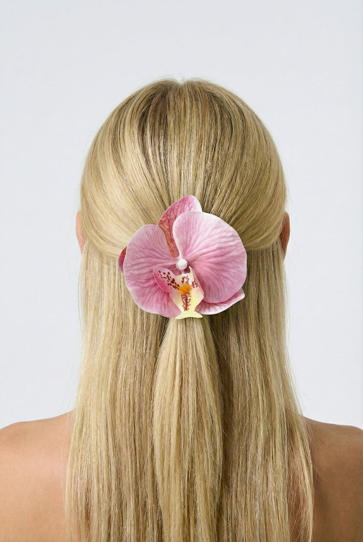 Person with pink orchid hair clip in blonde hair against a white background