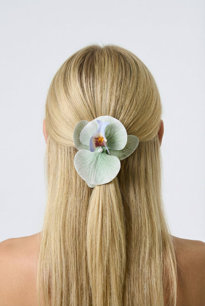 Woman with long blonde hair wearing a light blue orchid hair clip against a white background