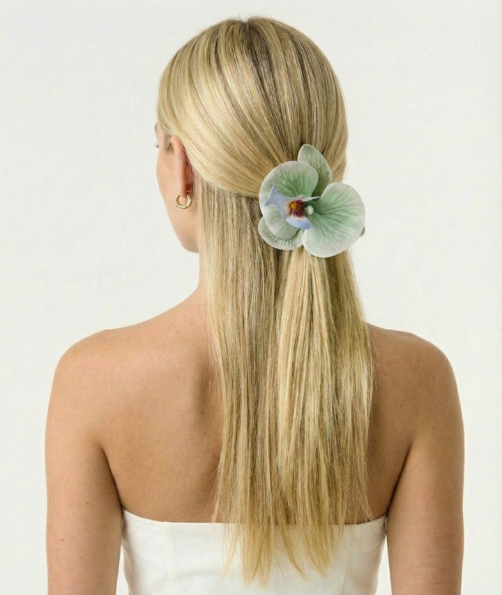 Woman with long blonde hair featuring a decorative flower hairpiece on a white background