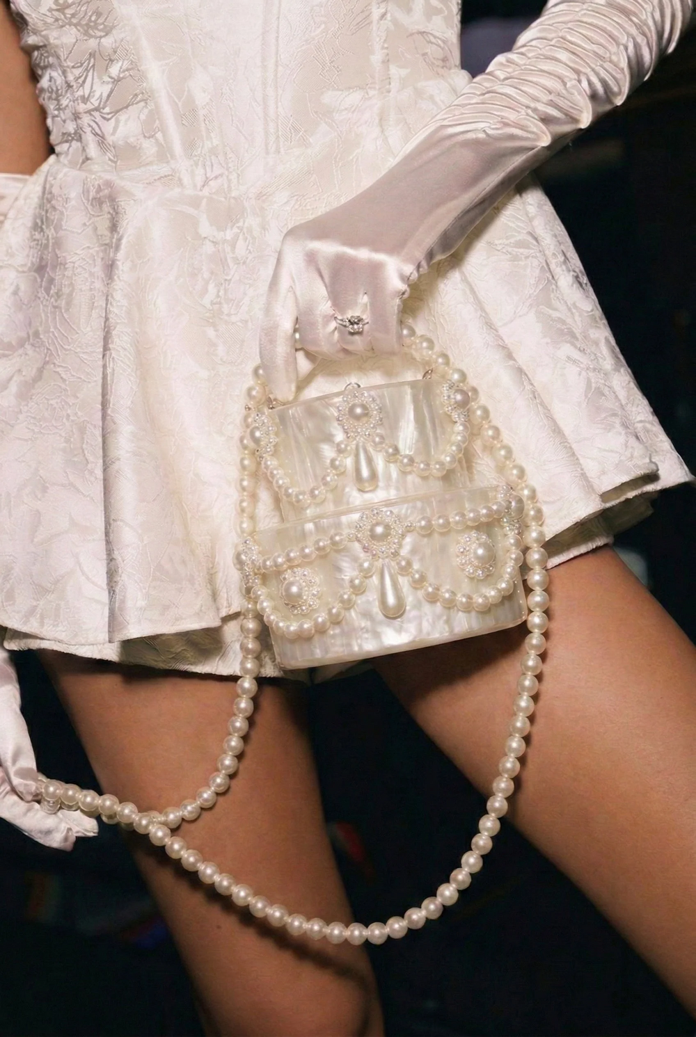 White lace dress with a matching handbag and pearl strap on a dark background